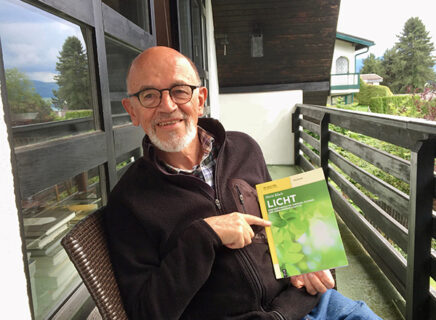 Prof. Dr. i. R. Horst Kisch sitzt auf seinem Balkon und hält sein Buch in die Kamera.