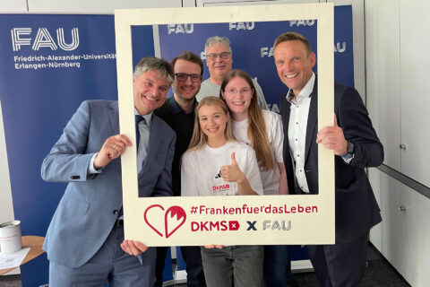 Das Foto zeigt den Präsidenten der FAU sowie fünf weitere Personen, die einen großen Rahmen hochhalten. Sie lächeln in die Kamera und werben auf dem Rahmen dafür sich typisieren zu lassen.